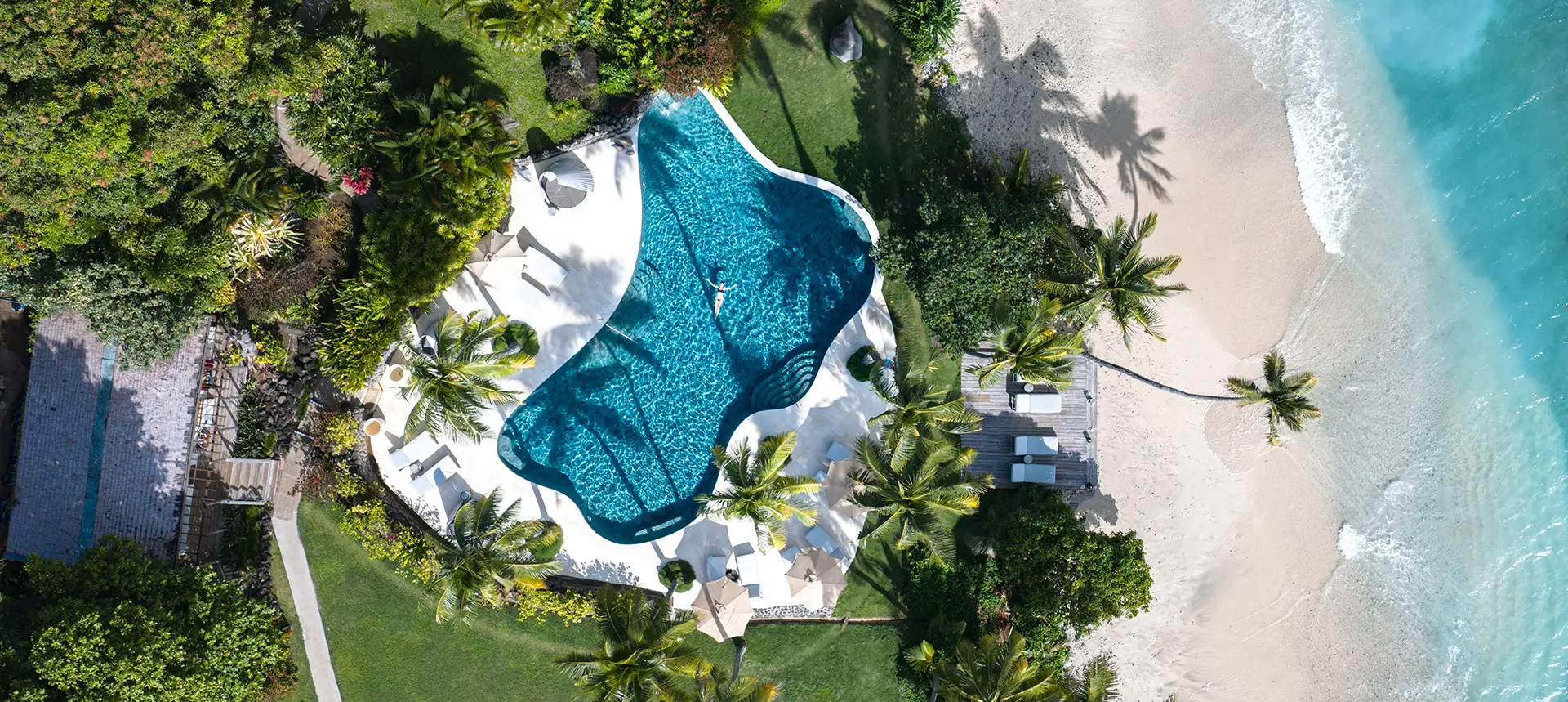 Aerial view of the adults-only Royal Davui Island Resort in Fiji showing the beachfront pool surrounded by palm trees and turquoise lagoon waters.