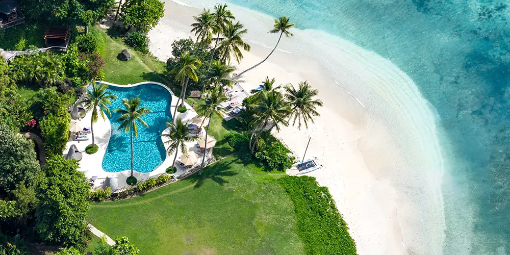 Aerial view of Royal Davui Island Resort’s adults-only beachfront pool surrounded by palm trees and turquoise lagoon, showing the privacy of the private island.
