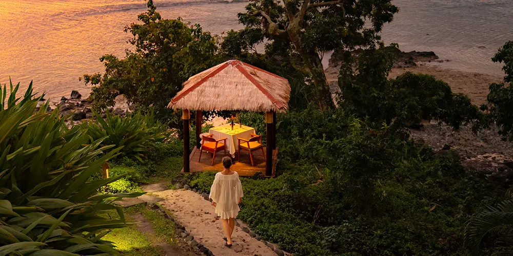 Woman walking to a private sunset dining pavilion overlooking the ocean at Royal Davui Island Resort, an adults-only couples retreat in Fiji.